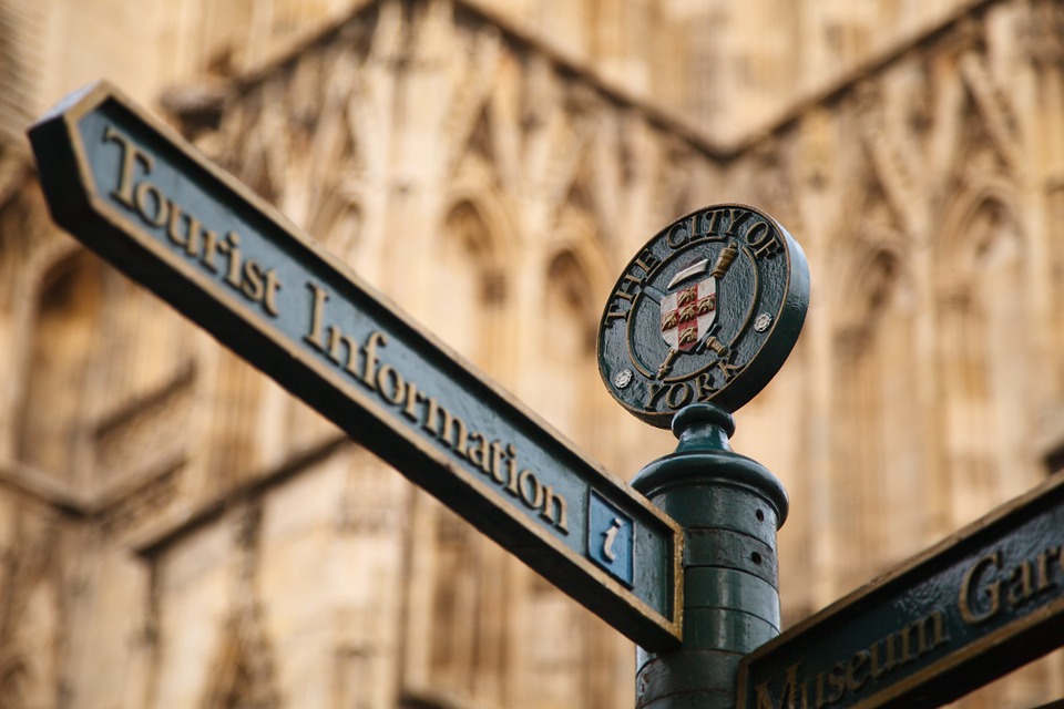 A sign metal sign post in front of a church in York, England pointing to Tourist Information.