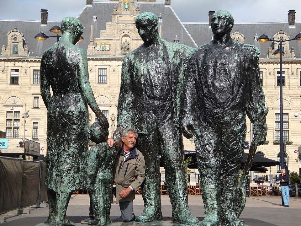 A man poses on one knee in the middle of a metal statue of two men, a woman, and a child.