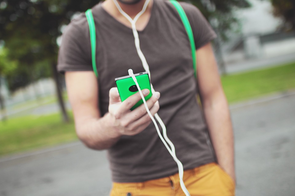 The burred torso of a man with headphones on holding his in-focus phone in front of him.