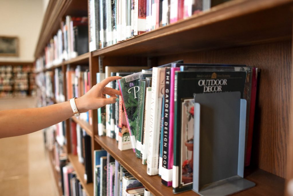 Library shelving full of books. A hand is removing one of the books from the shelf.