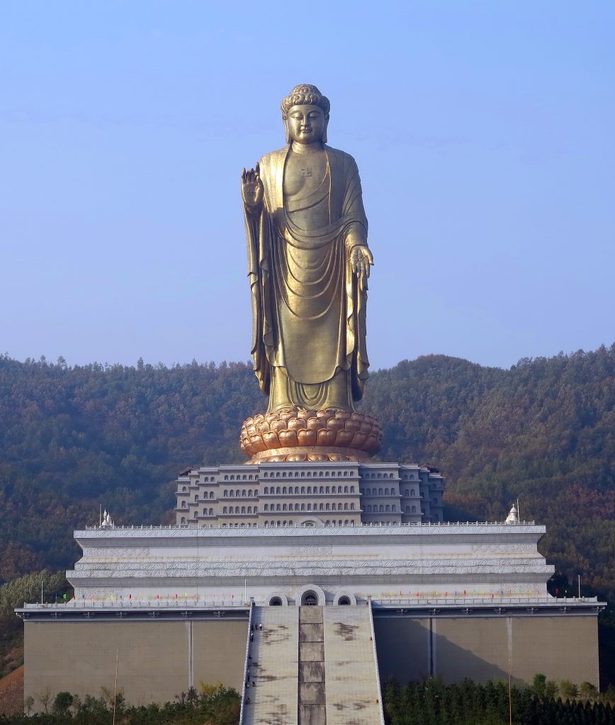 The Spring Temple Buddha statue against a clear blue sky. Including the temple building it stands on and the stairs leading up to the temple.