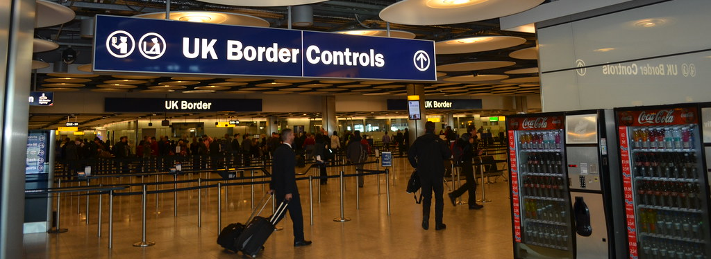 Lines of travelers at airport customs under a sign reading "UK Border Controls"