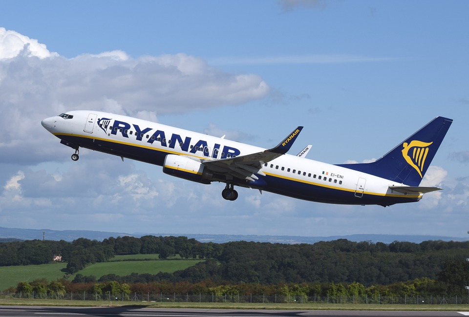 A RyanAir plane taking off with green fields and forests below.