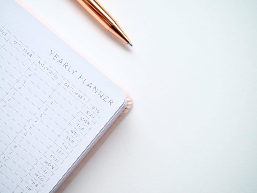 The corner of a yearly planner book with some dates visible and the tip of a pen.