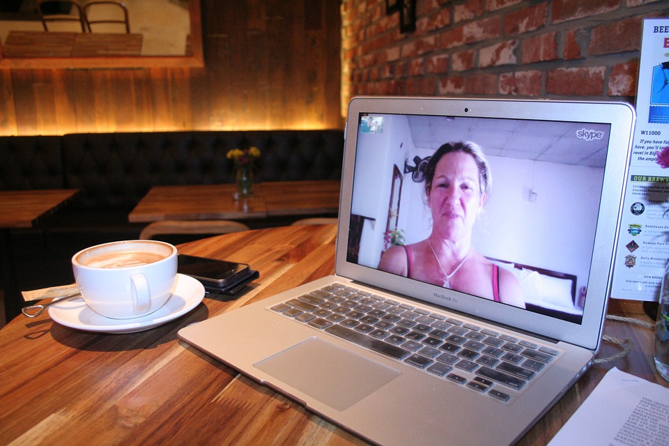 A laptop sitting on a table next to a cup of coffee. A Skype video chat with a blond woman is fullscreen.