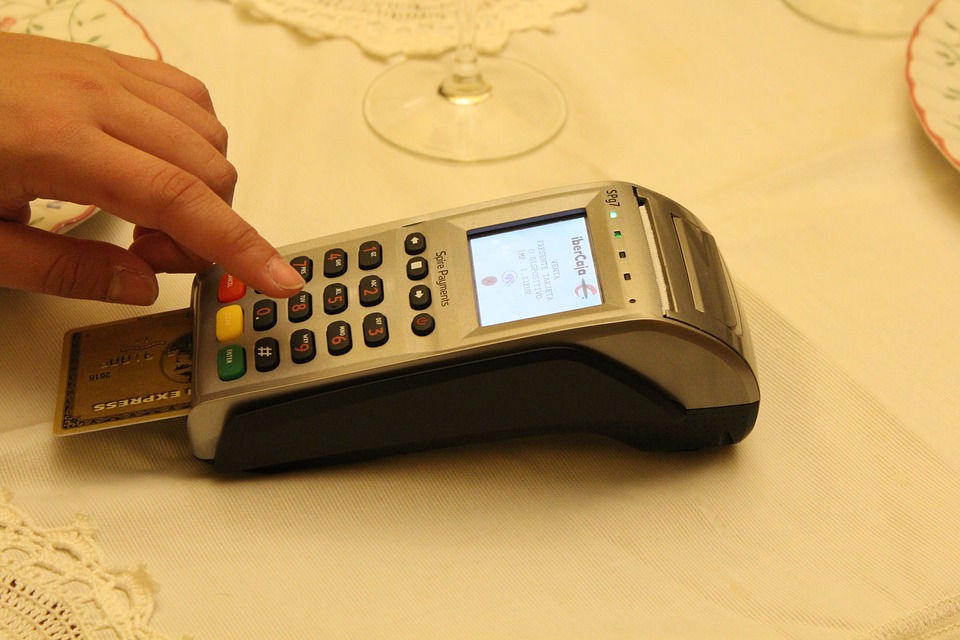 Credit card payment terminal sitting on a restaurant table with a credit card in the chip reader. A hard is pressing a button.