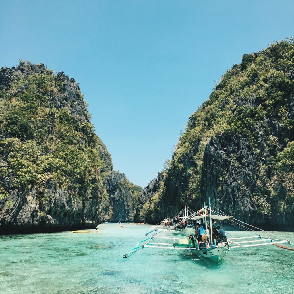 Tropical water with several boats surrounded by high cliffs in the Philippines.