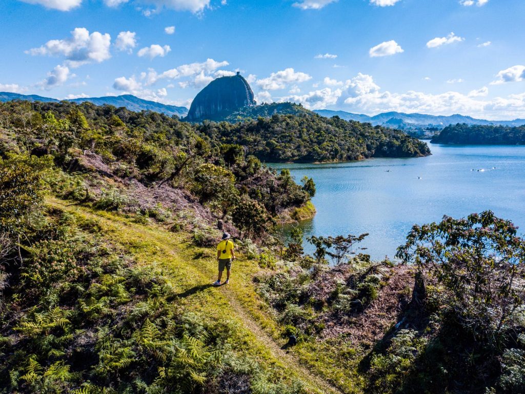 Someone walking along a Colombian path above the water with mountains in the background.