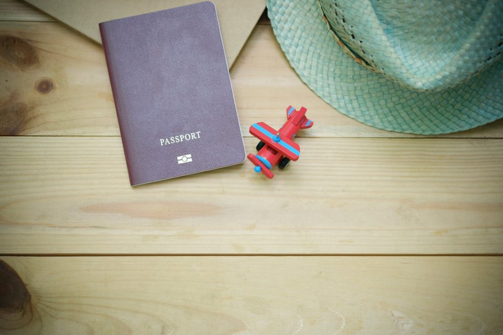 Wooden table with a passport, sun hat, and toy airplane.