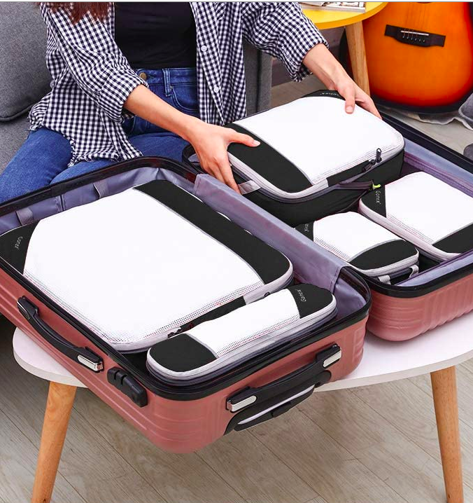 An open suitcase full of packing cubes. Hands are placing the last packing cube neatly in the suitcase.