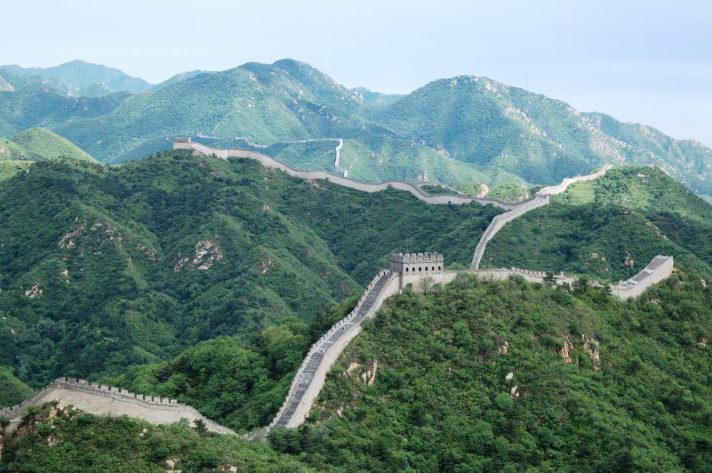 The Great Wall of China zig-zagging across green hills.