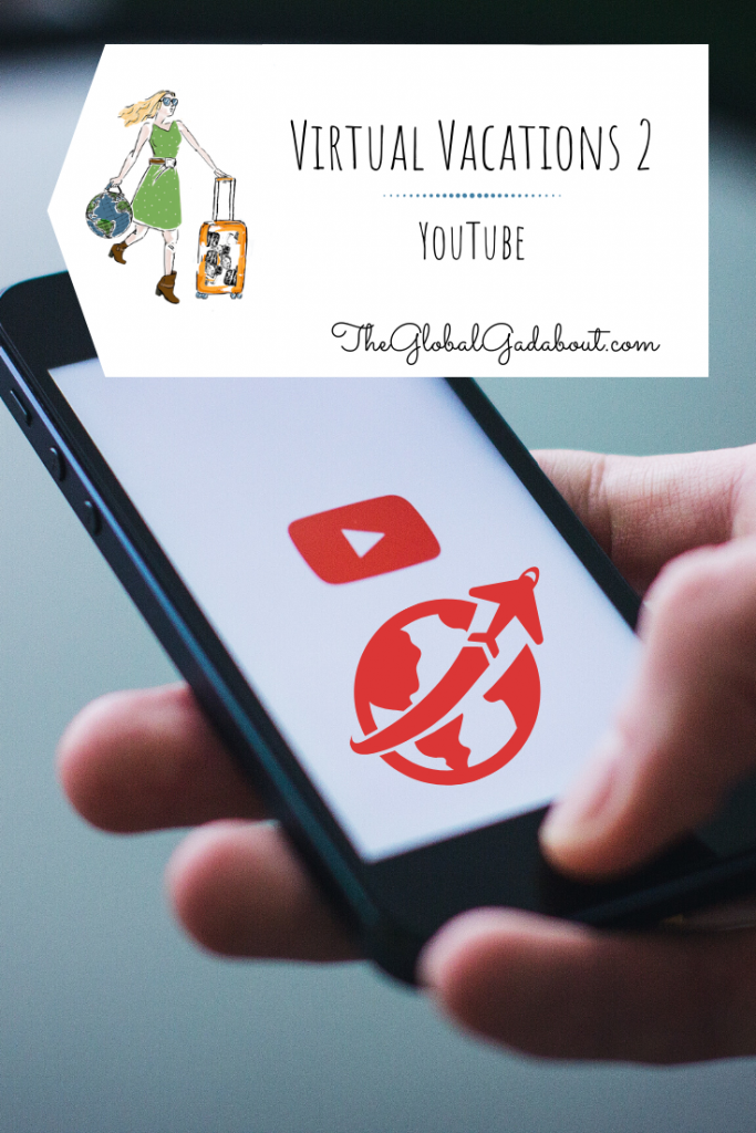 A hand holding a phone with a YouTube "play" symbol and an airplane circling the world graphic on the screen. A white luggage tag shaped box is superimposed at the top with The Global Gadabout symbol and the words "Virtual Vacations 2: YouTube" and "TheGlobalGadabout.com".