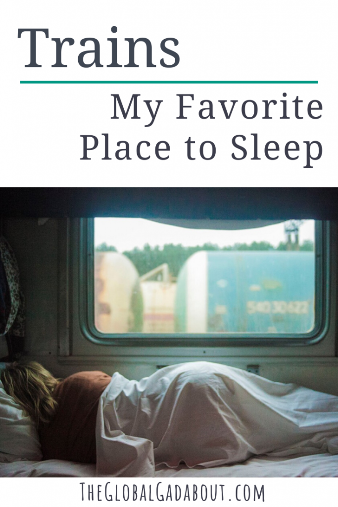 White background with the words "Trains: My Favorite Place to Sleep" and "TheGlobalGadabout.com". Between the two phrases is a photo of a woman sleeping on a train, her back to the camera, covered by a sheet with a large window above her.