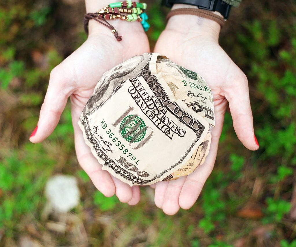 Two hands hold out a large ball of money. A US $100 bill is prominent.