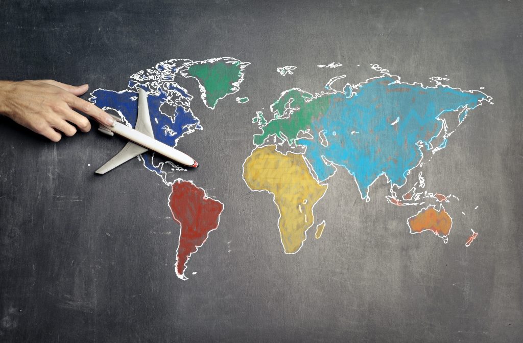 A colorful world map drawn on a chalkboard. A hand is push a toy airplane across the map.