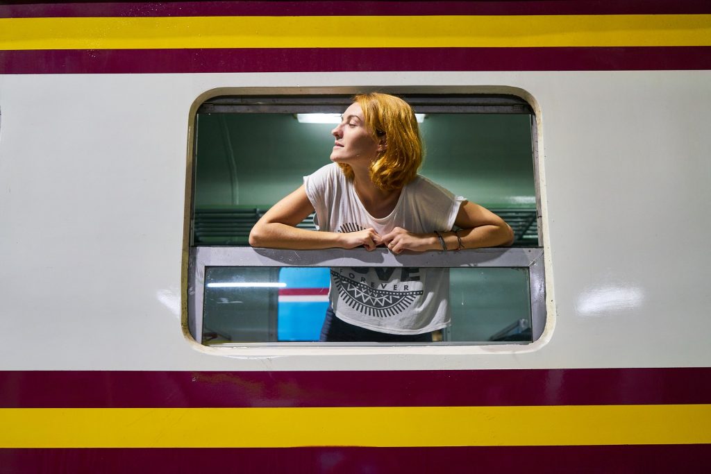 A woman leans out the window of a train, looking into the distance.