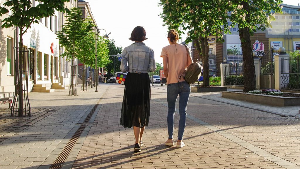 Two women walking down a tree-lined street.